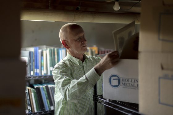A person in a green plaid dress shirt looking through files in a box. 